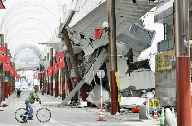 In this Saturday, April 16, 2016, file photo, a cyclist looks at a shopping arcade destroyed by an earthquake in Kumamoto city, southern Japan. The powerful earthquake struck southwestern Japan early Saturday, barely 24 hours after a smaller quake hit the same region. (Kyodo News via AP) JAPAN OUT, MANDATORY CREDIT