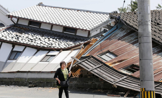 A woman walks past houses destroyed by Thursday's earthquake in Mashiki, Kumamoto prefecture, southern Japan, Friday, April 15, 2016. The powerful earthquake struck Thursday night, knocking down houses and buckling roads. (Naoya Osato/Kyodo News via AP) JAPAN OUT, MANDATORY CREDIT