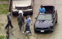 In this image made from a video provided by KABC-TV, two burglary suspects in blue shirts - one standing in the car and one at center left - greet onlookers when they ended the pursuit in a convertible Mustang in South Los Angeles, Thursday, April 7, 2016. The bizarre chase on rainy Southern California streets and highways ended when the pair stopped the car in a South Los Angeles neighborhood, exchanged high-fives with onlookers and took selfies before officers arrived several minutes later and handcuffed them. (KABC-TV via AP) MANDATORY CREDIT TV OUT