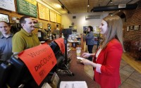 Molly Kepner, right, smiles after hearing the news of her discount from Tom Grover at The Works Bakery Cafe, Tuesday, April 12, 2016 in Concord, N.H. The New Hampshire bakery chain gave women a break in honor of Equal Pay Day charging them 79 percent of their bill. (AP Photo/Jim Cole)