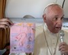 Pope Francis shows drawings made by children on his flight back to Rome following a visit to the Greek island of Lesbos, Saturday, April 16, 2016. Pope Francis gave Europe a provocative and concrete lesson in how to treat refugees Saturday by bringing home 12 Syrian Muslims aboard his charter plane after an emotional visit to the hard-hit Greek island of Lesbos. (Filippo Monteforte/Pool Photo via AP)