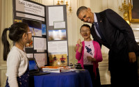 President Barack Obama laughs as he hugs Rebecca Yeung, 11, from Seattle, Wash., next to her sister Kimberly Yeung, 9, as they show him their homemade “spacecraft” that features a photograph of their late cat and is made of archery arrows and wood scraps  which they launched into the stratosphere via a helium balloon that records location coordinates, temperature, velocity, and pressure and reports the data back to the them, Wednesday, April 13, 2016, during the 2016 White House Science Fair at the White House in Washington. (AP Photo/Jacquelyn Martin)