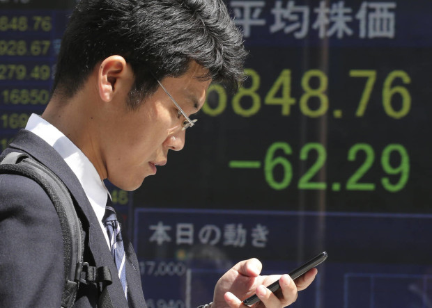 A man walks by an electronic stock board of a securities firm in Tokyo, Friday, April 15, 2016. Asian stocks mostly edged lower on Friday as investors assessed a report on Chinese quarterly economic growth while Japanese shares dropped after an earthquake. Market players were also watching for cues on currencies and other policies from a meeting in Washington, D.C., of financial ministers and central bank governors of the Group of 20 leading industrial nations. (AP Photo/Koji Sasahara)