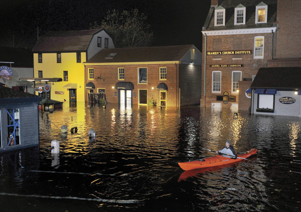 In this October 2012 photo, Jim Davis kayaks through waters flooding Bowen's Wharf after Superstorm Sandy in historic Newport, R.I. With scientists forecasting sea levels to rise by anywhere from several inches to several feet by 2100, historic structures and coastal heritage sites around the world are under threat. A multidisciplinary conference is scheduled to convene in Newport this week to discuss preserving those structures and neighborhoods that could be threatened by rising seas. (Dave Hansen/Newport Daily News via AP) MANDATORY CREDIT