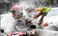 FILE - In this April 13, 2015 file photo, people riding on a motorbike react as a boy splashes water on them during the traditional Thai New Year celebrations or Songkran water festival in Bangkok. Thailand’s military government is putting a dampener on the annual nationwide water fight. Despite Thailand’s worst drought in 20 years, the junta says it has no intention of limiting the virtually around-the-clock water throwing that defines the three-day Songkran festival. Instead, it has decided to impose morality measures. (AP Photo/Sakchai Lalit,File)