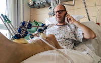 Walter Benjamin makes a phone call as he rests in his bed in Jette University Hospital in Brussels on Sunday, April 3, 2016. Benjamin survived the Brussels airport attack but lost a leg. In the days since Islamic State suicide bombers attacked the Brussels airport, survivor Walter Benjamin has been plugging away on Facebook from his hospital room, sharing his story, telling loved ones not to worry.    (AP Photo/Helene Franchineau)