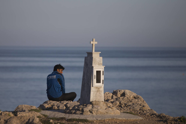 A Pakistani migrant stranded on the Greek island of Lesbos sits behind a memorial at a rocky sea side near the port of Mytilini, on Friday, April 15, 2016. Pope Francis will visit the island Saturday joined by Ecumenical Patriarch Bartholomew and the head of the Orthodox Church of Greece, Athens Archbishop Ieronymos II. During his six-hour stay, Francis will visit a camp on Lesbos where 2,300 migrants and refugees are being detained for deportation back to Turkey, under an agreement between Ankara and the European Union that human rights groups globally are railing against. (AP Photo/Petros Giannakouris)