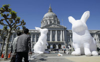 Pedestrians look toward large illuminated rabbits installed at Civic Center Plaza as part of an art piece entitled "Intrude" by Australian artist Amanda Parer, across from City Hall in San Francisco, Tuesday, April 5, 2016. To prevent the kind of vandalism that hit Super Bowl 50 artwork earlier this year, the bunnies will get 24-hour security from now until the exhibit ends on April 25. (AP Photo/Jeff Chiu)