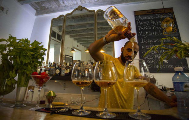 In this April 4, 2016 photo, Sandy, the barman at the upscale private "El De Enfrente" Bar serves drinks in Havana, Cuba. One month after President Obama’s visit, all eyes will be on Cuba’s Communist Party congress for the clearest picture yet of just how far the island’s leaders are willing to open their economy to deeper free market reforms, if at all. (AP Photo/Desmond Boylan)