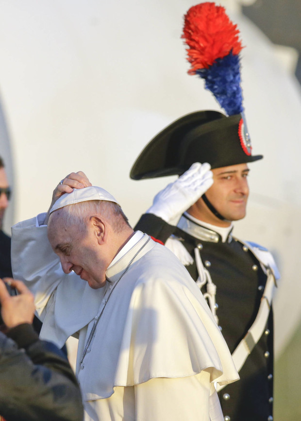 Pope Francis holds his skull cap as he boards an airplane at Rome's Fiumicino airport, Saturday, April 16, 2016, on his way to the Greek island of Lesbos, The Pontiff will visit the island Saturday joined by Ecumenical Patriarch Bartholomew and the head of the Orthodox Church of Greece, Athens Archbishop Ieronymos II, a mission human rights groups hope will highlight the plight of refugees who fled their war-ravaged homes only to be denied entry to Europe. (AP Photo/Gregorio Borgia)