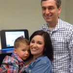 Kaylyn Milligan holding her 2-year-old son Owen and Dr. Jimmy Bennett stand by the new Illumina NextSeq gene sequencing machine. (Colleen O'Brien/KIRO Radio)