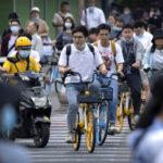 
              People ride bicycles across an intersection during rush hour in Beijing, Friday, July 2, 2021. A small but visible handful of urban Chinese are rattling the ruling Communist Party by choosing to "lie flat," or reject high-status careers, long work hours and expensive cities for a "low-desire life." That clashes with party ambitions to make China a wealthier consumer society. (AP Photo/Mark Schiefelbein)
            