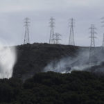 
              FILE - In this Oct. 10, 2019, file photo, a helicopter drops water near power lines and electrical towers while working at a fire on San Bruno Mountain near Brisbane, Calif. Pacific Gas & Electric plans to bury 10,000 miles of its power lines in an effort to prevent its fraying grid from sparking wildfires when electrical equipment collides with millions of trees and other vegetation sprawling across its drought-stricken service. (AP Photo/Jeff Chiu, File)
            