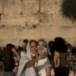 
              Women pose for a selfie at the Western Wall, the holiest site where Jews can pray, in the shadow of the Mughrabi Bridge, a wooden pedestrian bridge connecting the wall to the Al Aqsa Mosque compound, in Jerusalem's Old City, Tuesday, July 20, 2021. The rickety bridge allowing access to Jerusalem's most sensitive holy site is at risk of collapse, according to experts. But the flashpoint shrine's delicate position at ground-zero of the Israeli-Palestinian conflict has prevented its repair for more than a decade. (AP Photo/Maya Alleruzzo)
            