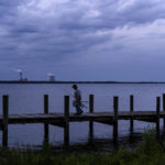 
              A fisherman walks along a dock on the St. Johns River as a coal-fired power plant stands in the background, in Palatka, Fla., Wednesday, April 14, 2021. After months in a prison cell, Warren Williams longed to fish the St. Johns again. He looked forward to spending days outdoors in his landscaping job, and to writing poems and music in his free time. (AP Photo/David Goldman)
            