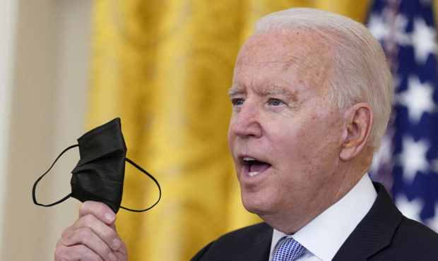 President Joe Biden holds up a mask as he announces from the East Room of the White House in Washin...