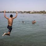 
              A youth jumps in the sea at a beach of Kavouri suburb, southwest of Athens, on Friday, July 30, 2021. Greek authorities ordered additional fire patrols and infrastructure maintenance inspections Friday as the country grappled with a heat wave expected to last more than a week, with temperatures expected to reach 42 C (107.6 F). (AP Photo/Yorgos Karahalis)
            