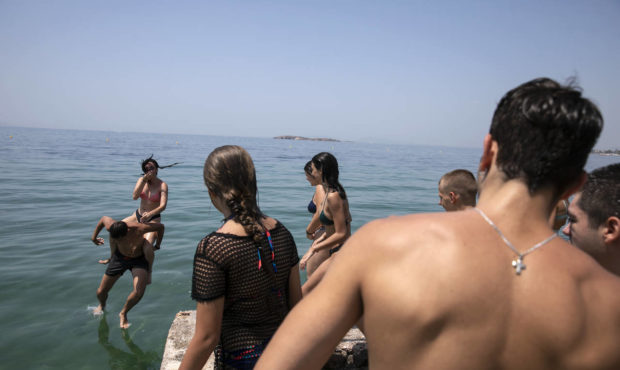 People jump in the sea at a beach of Kavouri suburb, southwest of Athens, on Friday, July 30, 2021....