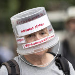 
              A demonstrator walks through Berlin-Charlottenburg with a plastic bucket placed on his head reading 'Absolutely safe against the stupidity virus', in Berlin, Sunday Aug. 1, 2021, during a protest against coronavirus restrictions. Hundreds have turned out in Berlin to protest the German government’s anti-coronavirus measures despite a ban on the gatherings, leading to arrests and clashes with police.  (Fabian Sommer/dpa via AP)
            