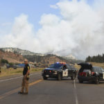 
              A plume of smoke rises from a wildfire as Cascade County sheriff's deputies prevent traffic from passing through along Highway 212 near Lame Deer, Mont., Wednesday, Aug. 11, 2021. The Richard Spring fire was spreading rapidly Wednesday as strong winds pushed it through rough, forested terrain.  In southeastern Montana, communities in and around the Northern Cheyenne Indian Reservation were ordered to evacuate as the Richard Spring Fire grew amid erratic winds. The dangerous fires are among some 100 large blazes burning across 15 states. Most are in the West, where historic drought conditions have left lands parched. (AP Photo/Matthew Brown)
            