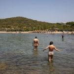 
              Swimmers walk into the sea at a beach of Kavouri suburb, southwest of Athens, on Friday, July 30, 2021. Greek authorities ordered additional fire patrols and infrastructure maintenance inspections Friday as the country grappled with a heat wave expected to last more than a week, with temperatures expected to reach 42 C (107.6 F). (AP Photo/Yorgos Karahalis)
            