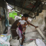 
              A woman carries her child as she walks in the remains of her home destroyed by Saturday´s  7.2 magnitude earthquake in Les Cayes, Haiti, Sunday, Aug. 15, 2021. (AP Photo/Joseph Odelyn)
            