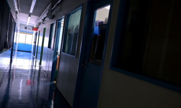 A hallway is empty with most of the lights off and one classroom light still on at a school in New ...