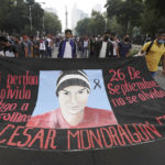 
              Supporters and relatives of 43 missing university students hold a banner with the likeness of one of the missing students, as they march on the seventh anniversary of their disappearance, in Mexico City, Sunday, Sept. 26, 2021. Relatives continue to demand justice for the Ayotzinapa students who were allegedly taken from the buses by the local police and handed over to a gang of drug traffickers. (AP Photo/Marco Ugarte)
            