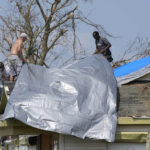 
              Gary Johnston, left, Grant Boughamer, center, and Jose Garcia, right, place a tarp on a roof damaged by Hurricane Ida, Thursday, Sept. 2, 2021, in Golden Meadow, La. (AP Photo/David J. Phillip)
            