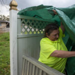 
              Vickey Schneider secures a tarp around the edge of her family's roof in Kenner, La., where they also keep their generator, Monday, Sept. 6, 2021, a week after Hurricane Ida swept through the area. (Chris Granger/The Times-Picayune/The New Orleans Advocate via AP)
            