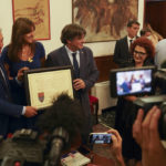 
              Catalan separatist leader Carles Puigdemont, right, flanked by Speaker of the Catalan Parliament Laura Borras exchanges gifts with Mayor of Alghero Mario Conoci, left, in Alghero, Sardinia, Italy, Saturday, Sept. 25, 2021. Puigdemont was visiting the city hall after he took a leisurely walk in the Sardinian city, waving to supporters, a day after a judge freed him from jail pending a hearing on his extradition to Spain, where the political firebrand is wanted for sedition. (AP Photo/Andrea Rosa)
            