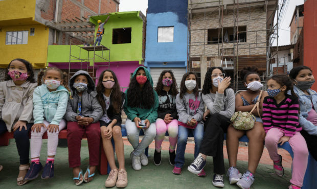 Workers paint the facades of residences in the Paraisopolis favela, as children sit on a bench duri...