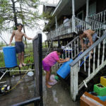 
              Lerryn Brune, 10, center, Terren Dardar, 17, right, and Dayton Verdin, 14, move barrels of rainwater they collected from Tropical Storm Nicholas, in the aftermath of Hurricane Ida in Pointe-aux-Chenes, La., Tuesday, Sept. 14, 2021. They have had no running water since the hurricane, and collected 140 gallons of rainwater in two hours from the tropical storm, which they filter and pump into their house for showers. (AP Photo/Gerald Herbert)
            