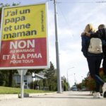 
              A couple walk past a poster showing a slogan in Perly near Geneva, Saturday Sept. 25, 2021. Voters in Switzerland will decide Sunday whether to allow same-sex marriages in the rich Alpine country, one of the few in Western Europe where gay and lesbian couples do not already have the right to wed. Opponents have argued that replacing civil partnerships with full marriage rights somehow would undermine families based on a union between one man and one woman. (Salvatore Di Nolfi/Keystone via AP)
            