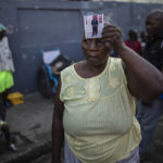 
              Twice displaced due to the country's escalating violence, Marie Jaquesmal poses with a portrait of her son Michel, who went missing during an assault lead by police, in Port-au-Prince, Haiti, Thursday, Sept. 16, 2021. With 139 houses set fire behind her, she lost track of her 28-year-old son, who is deaf and cannot speak.  "I don't know if he is dead or alive, the only thing I saw is that those men were policemen."  (AP Photo/Rodrigo Abd)
            