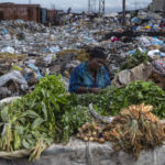 
              A woman selling greens waits for customers in the Croix des Bosalles market in Port-au-Prince, Haiti, Wednesday, Sept. 22, 2021. The floor of the market is thick with decomposing trash and, in some places, small fires of burning trash. (AP Photo/Rodrigo Abd)
            