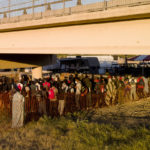 
              Migrants, many from Haiti, wait in lines to board buses under the Del Rio International Bridge, Friday, Sept. 24, 2021, in Del Rio, Texas. (AP Photo/Julio Cortez)
            