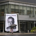 
              A woman walks by an image of federal bankruptcy judge Robert Drain that was installed by protesters in front of Purdue Pharma's headquarters, Wednesday, Sept. 1, 2021 in Stamford, Conn. The judge is preparing to rule on a plan for OxyContin maker Purdue Pharma to settle lawsuits brought by governments and others over its role in the opioid crisis. (AP Photo/Mark Lennihan)
            
