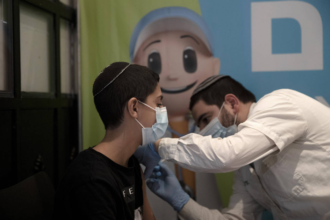A 14-year-old Israeli receives a booster shot of the coronavirus vaccine at Clalit Health Service's...