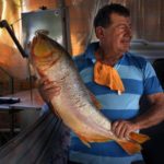 
              Fishmonger Dionisio Romero, 70, offers a "Dorado" to customers at his shop in Mariano Roque Alonso, Paraguay, Monday, Sept. 20, 2021. Romero is now buying fish more than 300 kilometers downstream because the ongoing drought has lowered the water to historical levels. (AP Photo/Jorge Saenz)
            