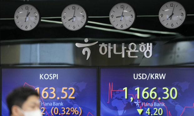 A currency trader walks by screens showing the Korea Composite Stock Price Index (KOSPI), left, and...