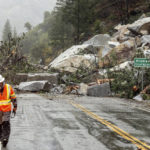 
              Caltrans maintenance supervisor Matt Martin walks by a landslide covering Highway 70 in the Dixie Fire zone on Sunday, Oct. 24, 2021, in Plumas County, Calif. Heavy rains blanketing Northern California created slide and flood hazards in land scorched during last summer's wildfires. (AP Photo/Noah Berger)
            