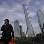 
              A woman wearing a face mask smokes as she walks by construction cranes stand near the skyscrapers at the Central Business District in Beijing, Monday, Oct. 18, 2021. China's economic growth sank in the latest quarter as a slowdown in construction and curbs on energy use weighed on its recovery from the coronavirus pandemic. (AP Photo/Andy Wong)
            