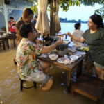 
              Customers of the riverside Chaopraya Antique Café enjoy themselves despite the extraordinary high water levels in the Chao Phraya River in Nonthaburi, near Bangkok, Thailand, Thursday, Oct. 7, 2021. The flood-hit restaurant has become an unlikely dining hotspot after fun-loving foodies began flocking to its water-logged deck to eat amid the lapping tide. Now, instead of empty chairs and vacant tables the “Chaopraya Antique Café” is as full as ever, offering an experience the canny owner has re-branded as “hot-pot surfing.” (AP Photo/Sakchai Lalit)
            