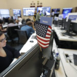 
              FILE – In this Oct. 17, 2018, file photo, a flag of the United State is shown between monitors as workers sit at their desks during a demonstration in the war room, where Facebook monitors election related content on the platform, in Menlo Park, Calif. From complaints whistleblower Frances Haugen has filed with the SEC, along with redacted internal documents obtained by The Associated Press, the picture of the mighty Facebook that emerges is of a troubled, internally conflicted company, where data on the harms it causes is abundant, but solutions are halting at best. (AP Photo/Jeff Chiu, File)
            