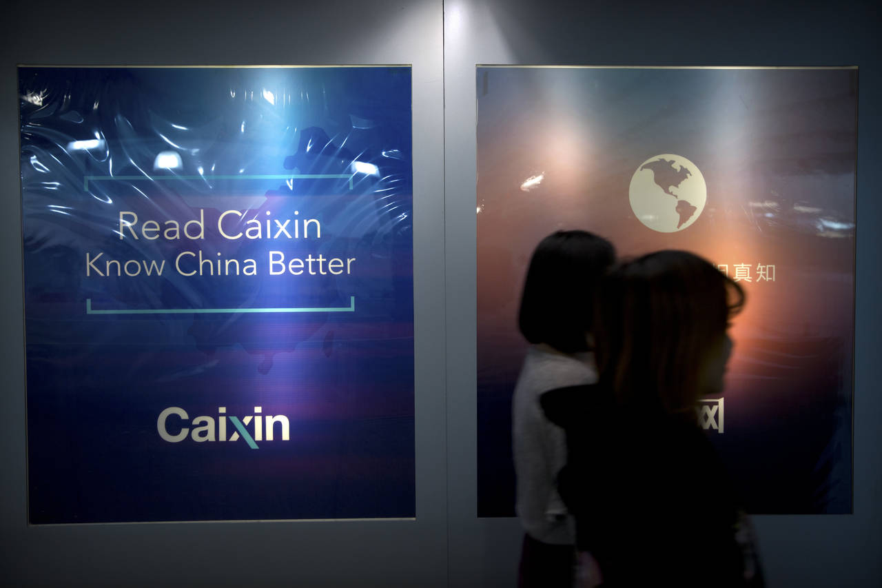 FILE - In this Jan. 18, 2018, file photo, staffers walk past a billboard reading "Read Caixin - Kno...