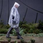 
              Alfred Giese, who drove in from sunny Indio, Calif. to attend the unveiling of the Anita Baldwin statue outside Le Méridien Hotel in Arcadia, stays dry under plastic during a rainstorm on Monday, Oct. 25, 2021. His wife Barbara is a distant relative of Anita Baldwin's half sister Clara. (Sarah Reingewirtz/The Orange County Register via AP)
            