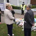 
              People gather by a floral tribute on the road leading to the Belfairs Methodist Church in Eastwood Road North, in Leigh-on-Sea, Essex, England, Saturday, Oct. 16, 2021. David Amess, a long-serving member of Parliament was stabbed to death during a meeting with constituents at a church in Leigh-on-Sea on Friday, in what police said was a terrorist incident. A 25-year-old man was arrested in connection with the attack, which united Britain's fractious politicians in shock and sorrow. (AP Photo/Alberto Pezzali)
            