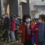 
              Women wearing face masks to help curb the spread of the coronavirus chat each other as they walk by masked residents line up to receive booster shots against COVID-19 at a vaccination site in Beijing, Monday, Oct. 25, 2021. A northwestern Chinese province heavily dependent on tourism closed all tourist sites Monday after finding new COVID-19 cases. (AP Photo/Andy Wong)
            