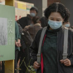 
              A woman wearing a face mask to help curb the spread of the coronavirus walks by a poster baring the words: "Epidemic protection" as masked residents line up to receive booster shots against COVID-19 at a vaccination site in Beijing, Monday, Oct. 25, 2021. A northwestern Chinese province heavily dependent on tourism closed all tourist sites Monday after finding new COVID-19 cases. (AP Photo/Andy Wong)
            